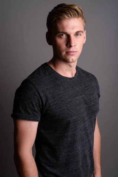 Jovem homem bonito com cabelo loiro vestindo camisa cinza contra gr — Fotografia de Stock