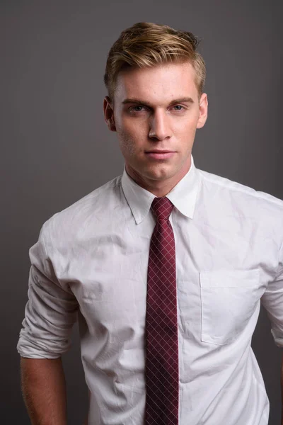 Ung snygg affärsman med blont hår mot grå backgrou — Stockfoto