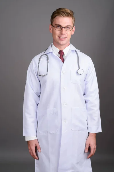 Jovem médico homem bonito com cabelo loiro contra backgroun cinza — Fotografia de Stock