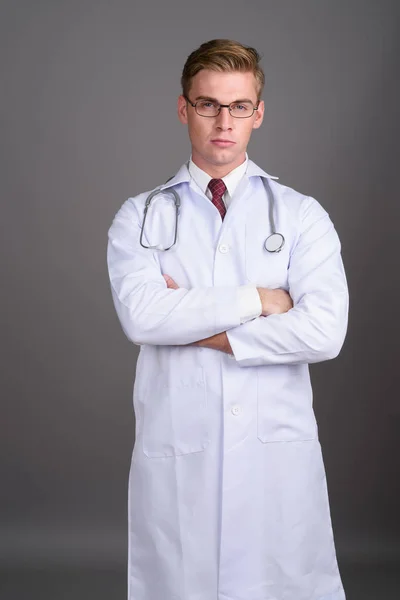 Молодий красивий чоловік лікар зі світлим волоссям проти сірого фону — стокове фото