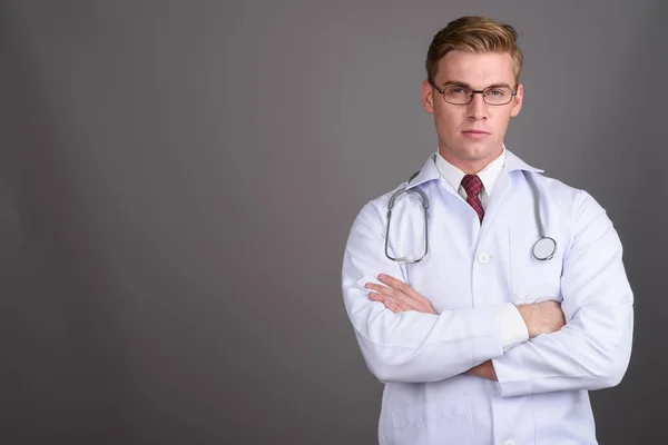Молодий красивий чоловік лікар зі світлим волоссям проти сірого фону — стокове фото