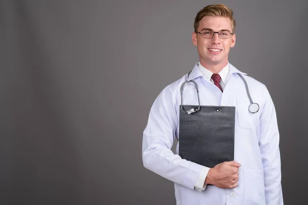 Doktor mladý pohledný muž s blond vlasy proti šedé poza — Stock fotografie