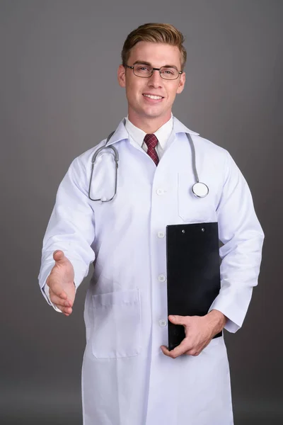 Pemuda tampan dokter dengan rambut pirang terhadap backgroun abu-abu — Stok Foto