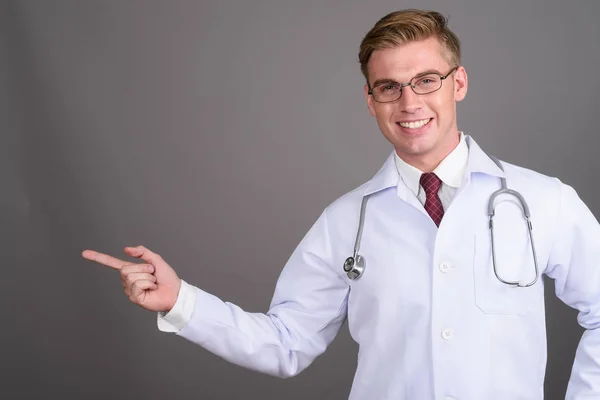 Young handsome man doctor with blond hair against gray backgroun — Stock Photo, Image