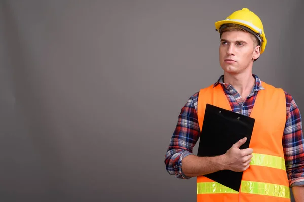 Joven hombre guapo trabajador de la construcción contra el fondo gris —  Fotos de Stock