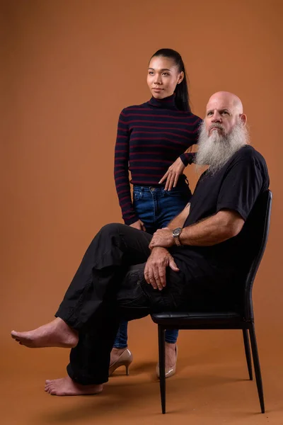 Mature bearded bald man with young Asian transgender woman