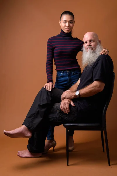 Mature bearded bald man with young Asian transgender woman