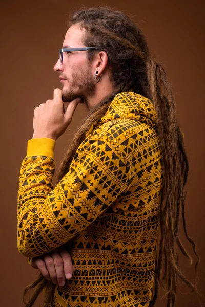 Joven hombre hispano guapo con rastas contra fondo marrón — Foto de Stock