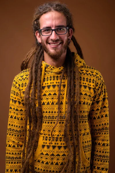 Jonge knappe man van de Hispanic met dreadlocks tegen bruin backgr — Stockfoto