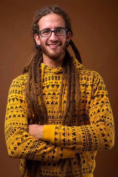 Joven hombre hispano guapo con rastas contra fondo marrón — Foto de Stock