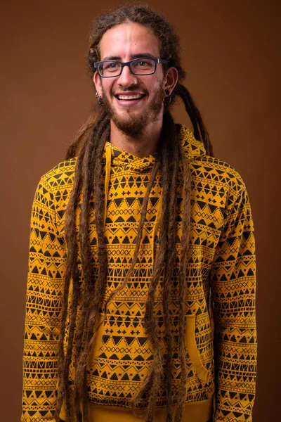 Joven hombre hispano guapo con rastas contra fondo marrón — Foto de Stock