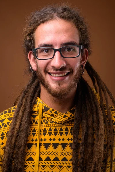 Joven hombre hispano guapo con rastas contra fondo marrón — Foto de Stock