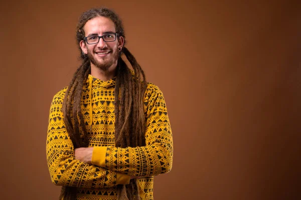 Junger hübscher hispanischer Mann mit Dreadlocks gegen braune Backgr — Stockfoto