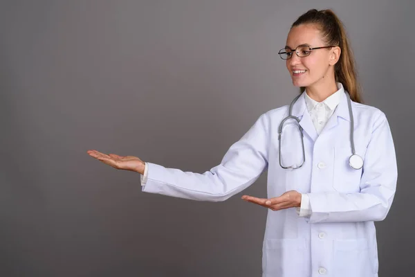 Joven hermosa mujer médico contra fondo gris — Foto de Stock