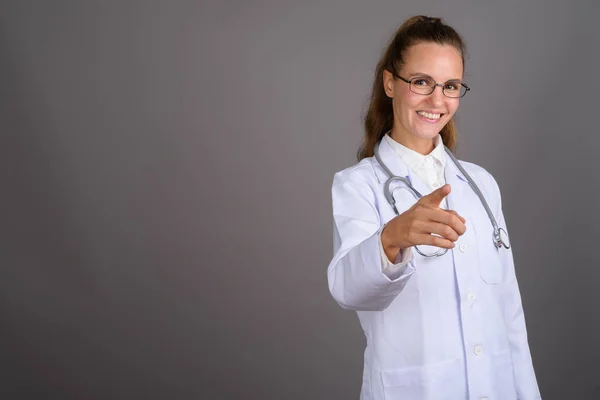 Joven hermosa mujer médico contra fondo gris — Foto de Stock