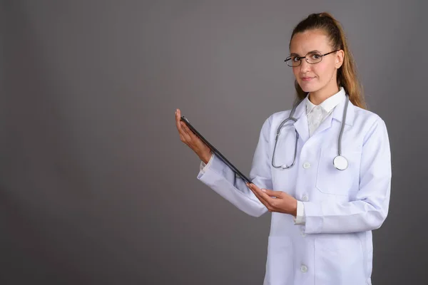 Joven hermosa mujer médico contra fondo gris — Foto de Stock