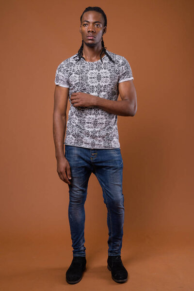 Studio shot of young handsome African man wearing gray shirt against brown background