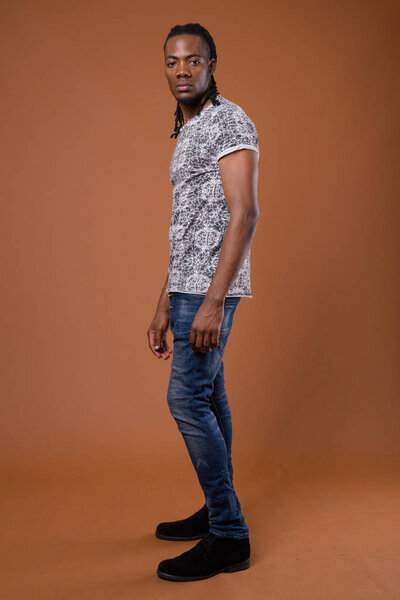 Studio shot of young handsome African man wearing gray shirt against brown background