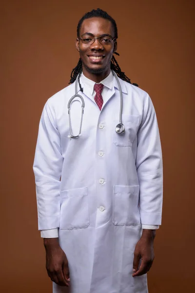 Молодой красивый африканский врач на коричневом фоне — стоковое фото