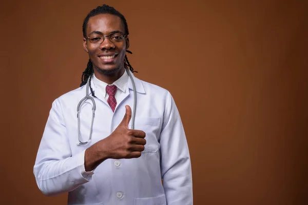 Young handsome African man doctor against brown background — Stock Photo, Image