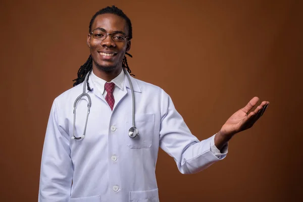 Young handsome African man doctor against brown background — Stock Photo, Image