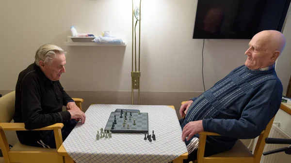 Dois homens idosos jogando xadrez enquanto relaxam em casa de repouso em T — Fotografia de Stock