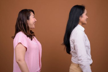 İki olgun Asyalı iş kadınının kahverengi arka planda çekilmiş bir stüdyo fotoğrafı.