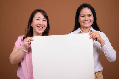 İki olgun Asyalı iş kadınının kahverengi arka planda çekilmiş bir stüdyo fotoğrafı.