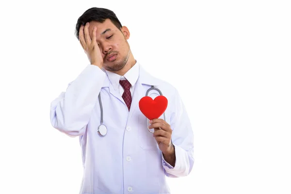 Studio shot of young Asian man doctor holding red heart while lo — Stock Photo, Image