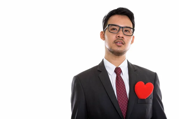 Studioaufnahme eines jungen asiatischen Geschäftsmannes, der mit rotem Herz denkt — Stockfoto