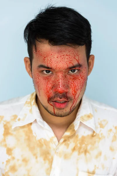Face of young crazy Asian man looking at camera with blood on fa