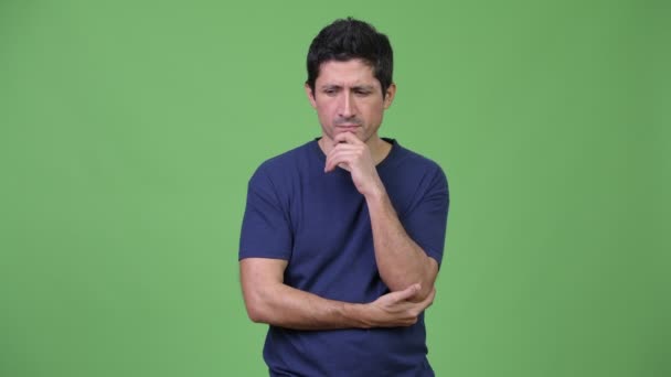 Серьезный латиноамериканец думает на зеленом фоне — стоковое видео