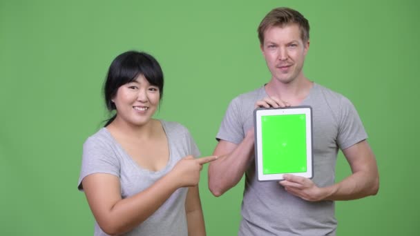 Unga lyckliga multietniska paret visar digitala tablett och ger tummen upp tillsammans — Stockvideo