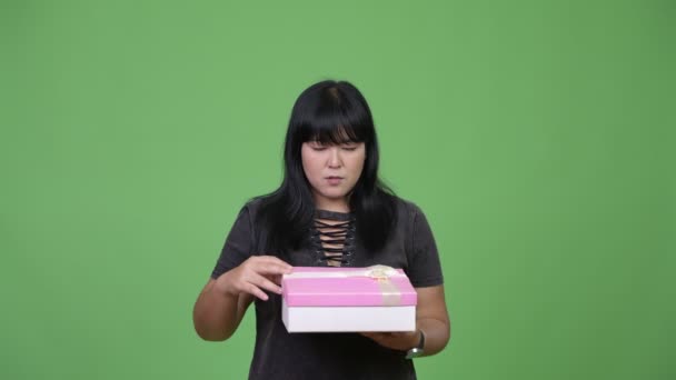 Hermosa mujer asiática con sobrepeso abriendo caja de regalo y mirando sorprendida — Vídeos de Stock