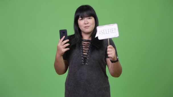 Hermosa mujer asiática con sobrepeso sosteniendo teléfono y selfie papel signo — Vídeos de Stock