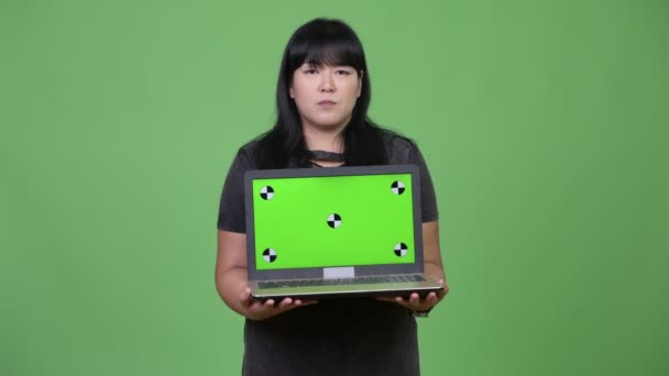 Heureuse femme asiatique en surpoids pensant tout en montrant ordinateur portable — Video