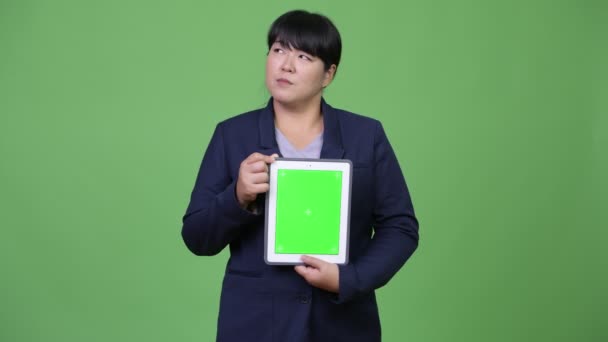 Happy overweight Asian businesswoman thinking while showing digital tablet — Stock Video