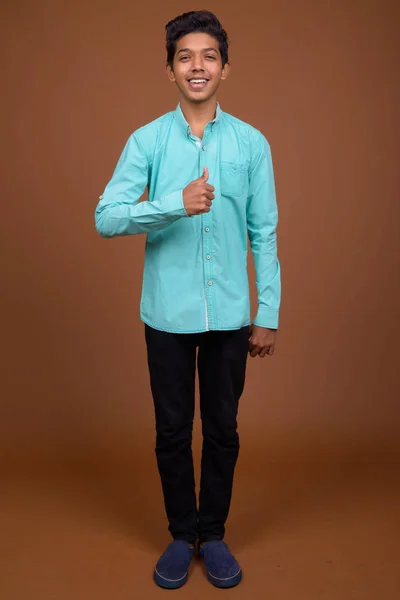 Jovem indiana menino vestindo azul camisa olhando inteligente contra marrom — Fotografia de Stock