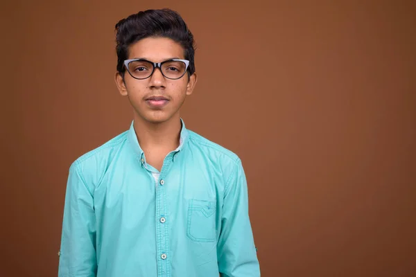 Joven chico indio con camisa azul mirando inteligente contra marrón — Foto de Stock