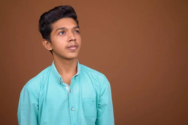 Молодой индийский мальчик в голубой рубашке выглядит умным против коричневого — стоковое фото