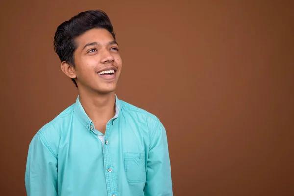 Joven chico indio con camisa azul mirando inteligente contra marrón — Foto de Stock