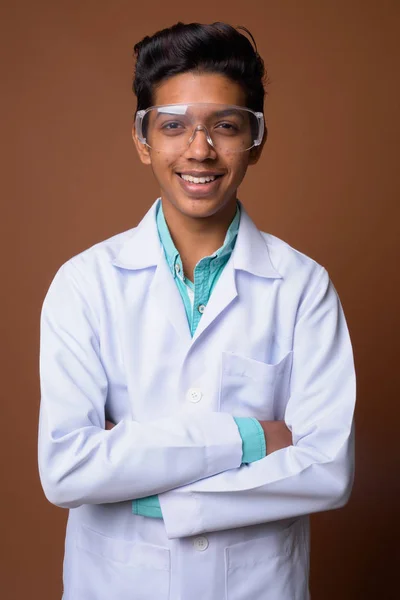 Young Indian boy doctor wearing protective glasses against brown — Stock Photo, Image