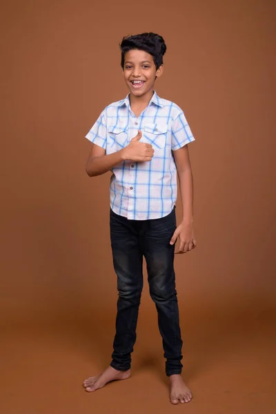 Молодой индийский мальчик в клетчатой рубашке против коричневой спинки — стоковое фото