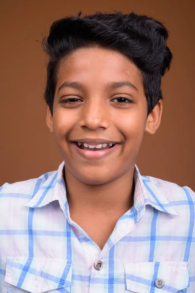 Молодой индийский мальчик в клетчатой рубашке против коричневой спинки — стоковое фото