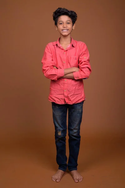 Menino indiano jovem vestindo roupas casuais inteligentes contra o bac marrom — Fotografia de Stock