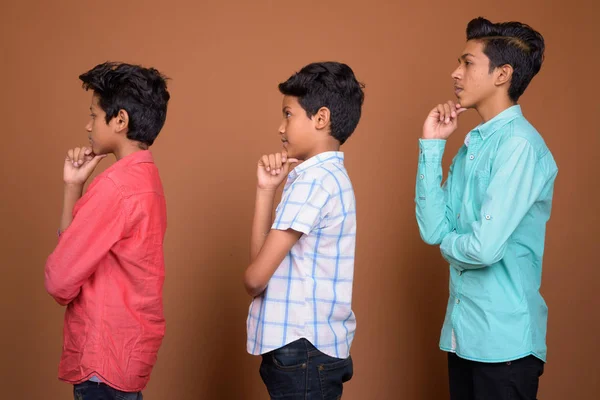 Drie jonge Indiase broers samen tegen bruine achtergrond — Stockfoto