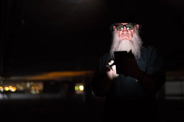 Mature bearded man using phone and looking suspicious — Stock Photo, Image