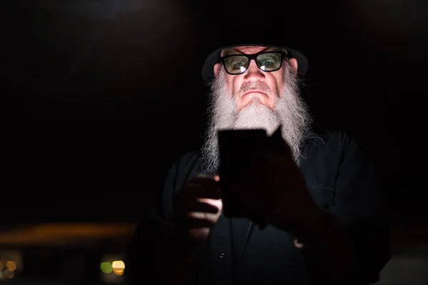 Mature bearded man using phone and looking suspicious — Stock Photo, Image