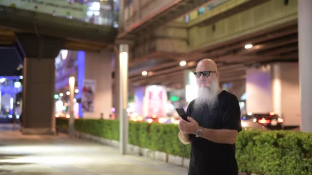 Зрелый лысый бородатый турист по ночам пользуется телефоном в городе — стоковое видео