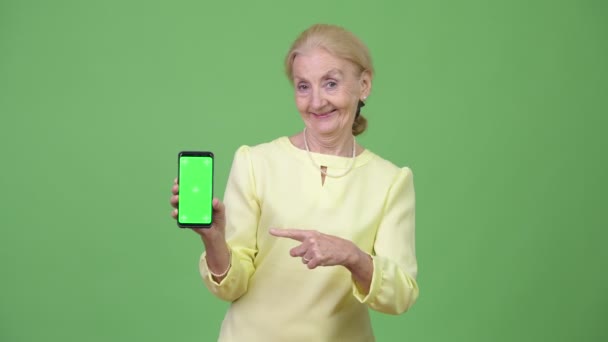 Beautiful happy senior businesswoman showing phone and giving thumbs up — Stock Video